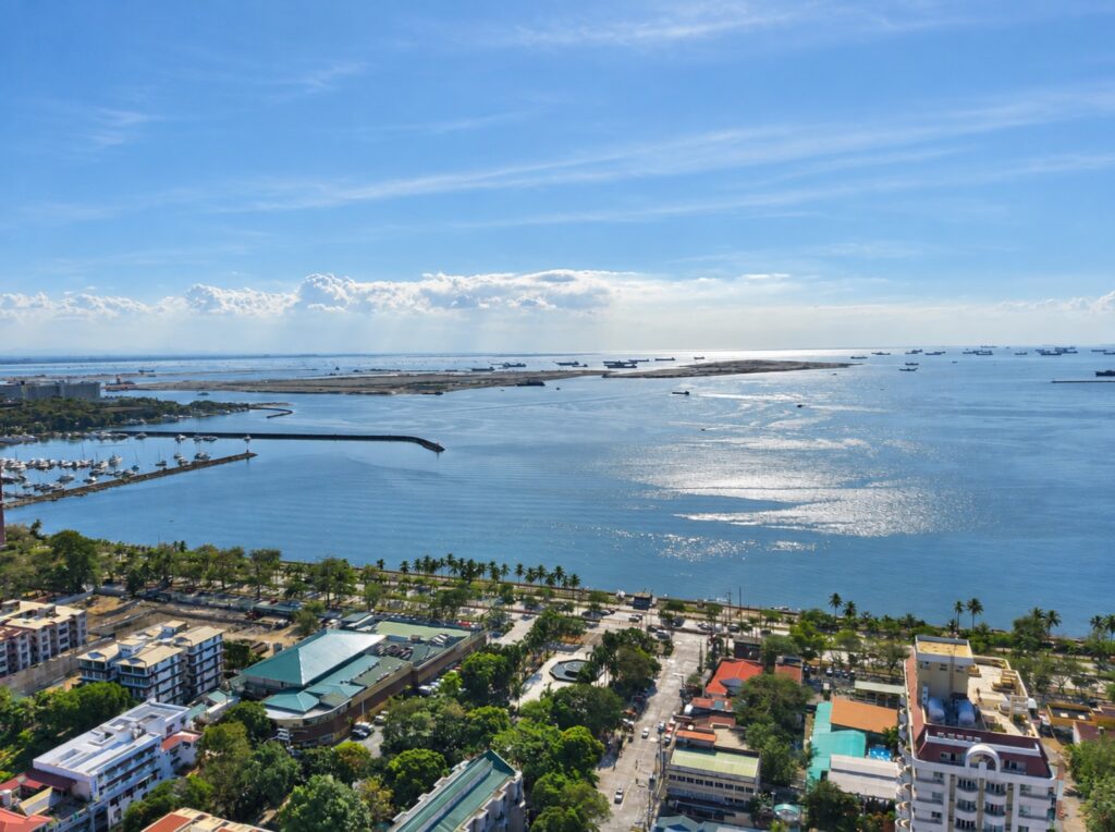 Blick über die Stadt und eine palmengesäumte Küste auf die Bucht mit Booten.